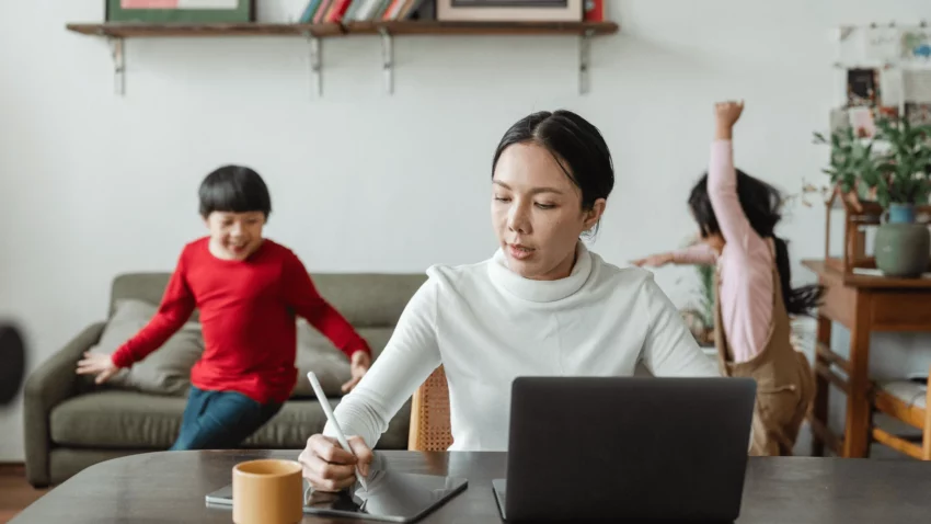 Une femme, maman de deux enfants, se trouve à son bureau à domicile, concentrée sur son travail sur l'ordinateur. À ses côtés, ses deux enfants en train de jouer, illustrant la réalité d'une maman en télétravail qui jongle avec les responsabilités professionnelles et familiales. Elle réussit à maintenir un équilibre tout en prenant soin de ses enfants et en gérant efficacement son travail à distance.