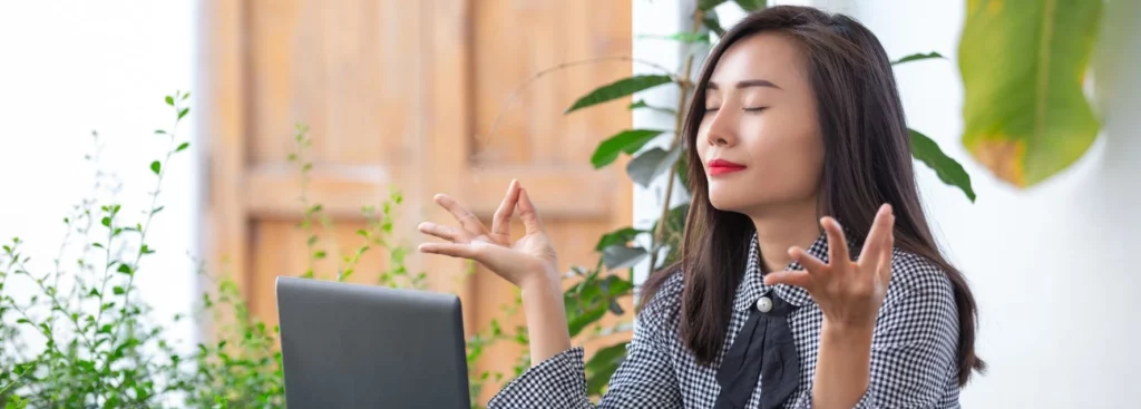 Une femme en télétravail trouve un moment de calme et de détente en pratiquant la méditation ou le yoga. Assise confortablement, elle se concentre sur sa respiration, cherchant l'apaisement au milieu des défis professionnels, démontrant l'importance de la gestion du stress dans l'environnement de travail à domicile.