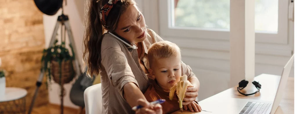 Une maman stressée, jonglant entre les exigences du travail et les besoins de son bébé tout en travaillant depuis la maison. Elle tient son bébé dans ses bras tout en s'efforçant de gérer ses tâches professionnelles, illustrant les défis du télétravail en conciliant la vie de parent et la vie professionnelle.